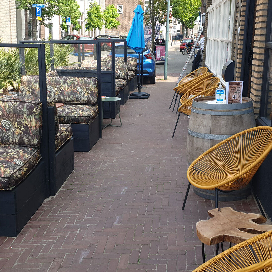 rieten stoeltjes en nisjes met zitbanken en felblauwe parasols op het terras van de wijnbar bij Restaurant Eindeloos in het Westland