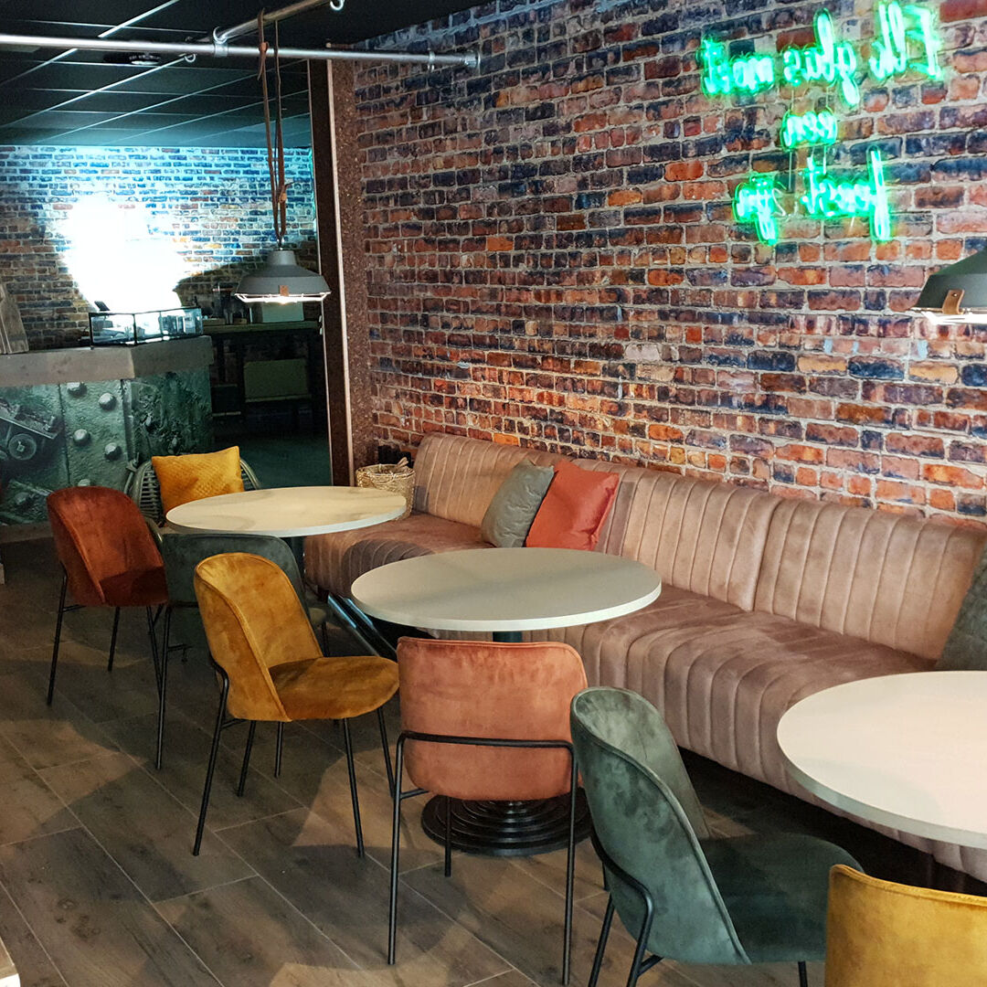 entree van restaurant Eindeloos in het Westland met een lange leren bank langs de muur en kleurrijke leren stoeltjes en witte tafels en een neontekst aan de muur in het Westland