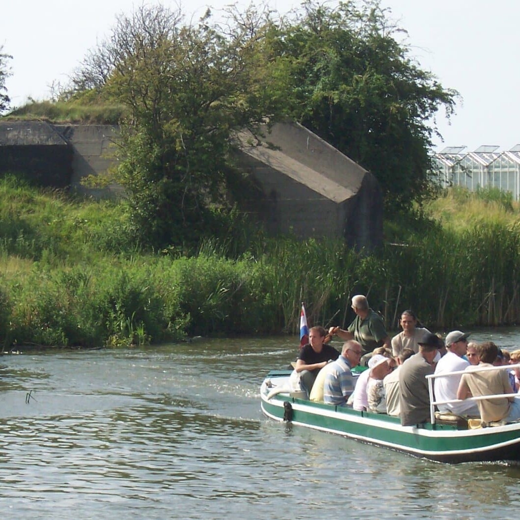 bootje met mensen aan boord vaart langs bunkers tussen de glazen kassen in het Westland
