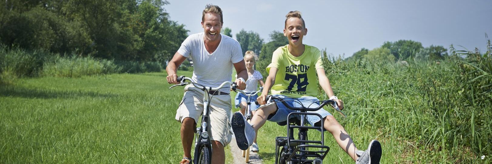 Lachende vader en zoon op een huurfiets in een groen landschap in het Westland