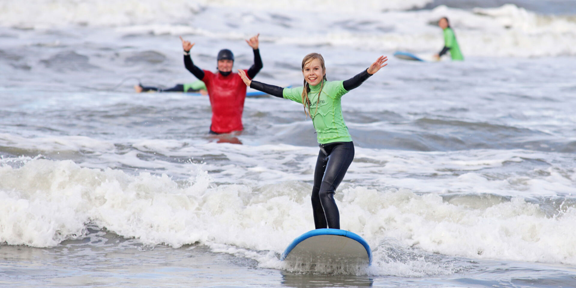 Jonge meisje in een zwarte wetsuit op een surfboard op zee tijdens een surfboardles bij Dreams Surfschool in het Westland