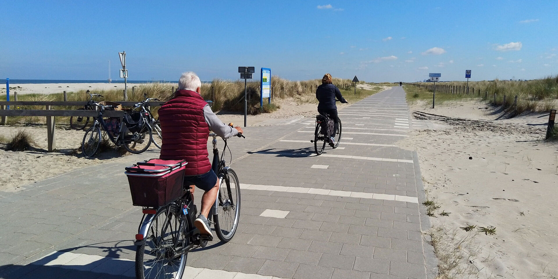 Oudere man en vrouw op de fiets op het fietspad door de duinen bij strandopgang Molenslag in het Westland