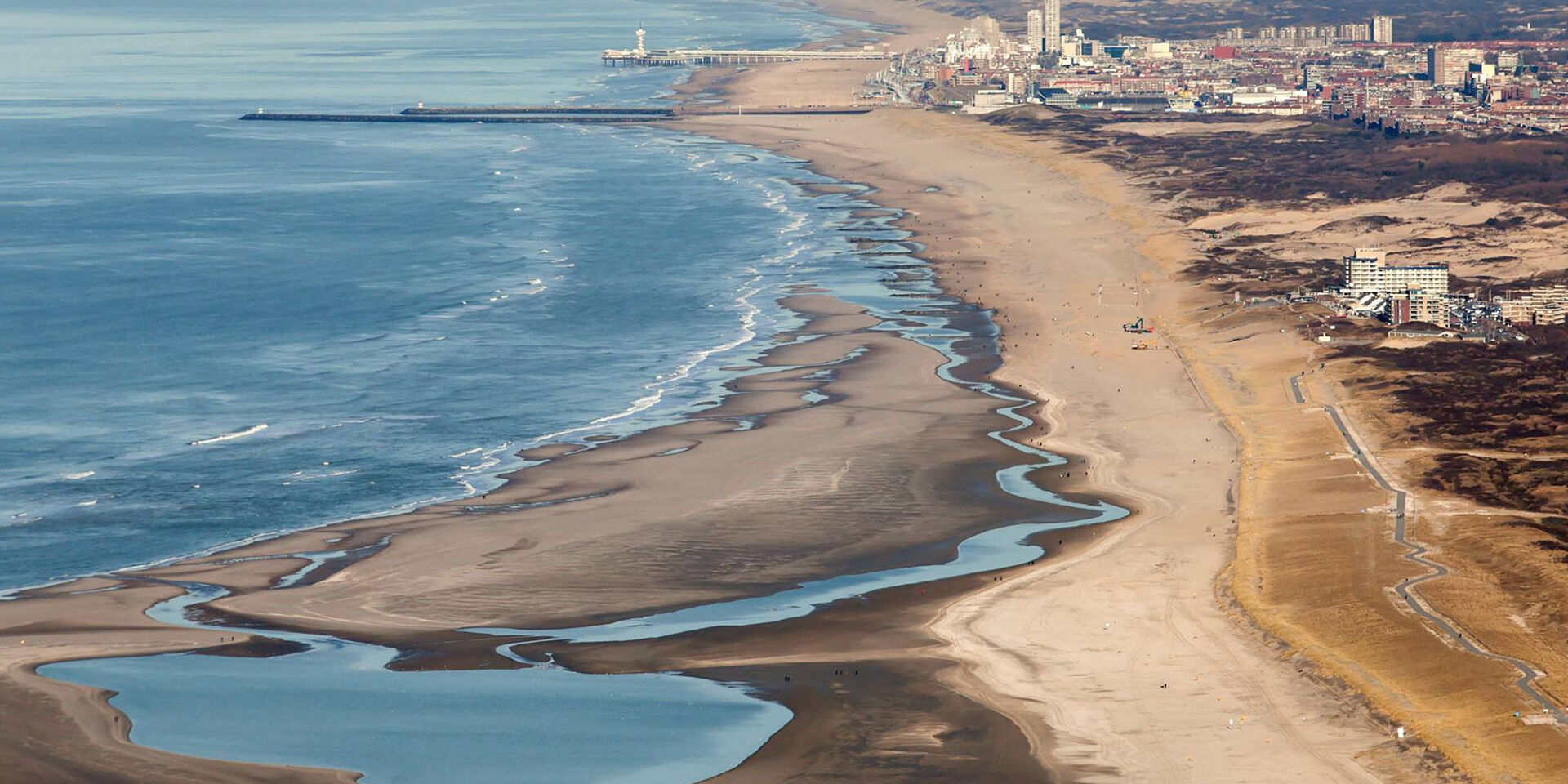 luchtfoto van de Zandmotor in het Westland van een breed strand met een binnenmeer en in de achtergrond Kijkduin