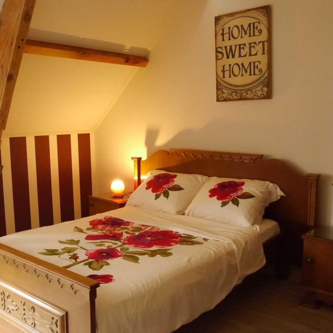 slaapkamer in B&B de Hooiberg in het Westland met ouderwets houten ledikant met een dekbed en kussens met rod rozen en een schilderij boven het bed met 'home sweet home'