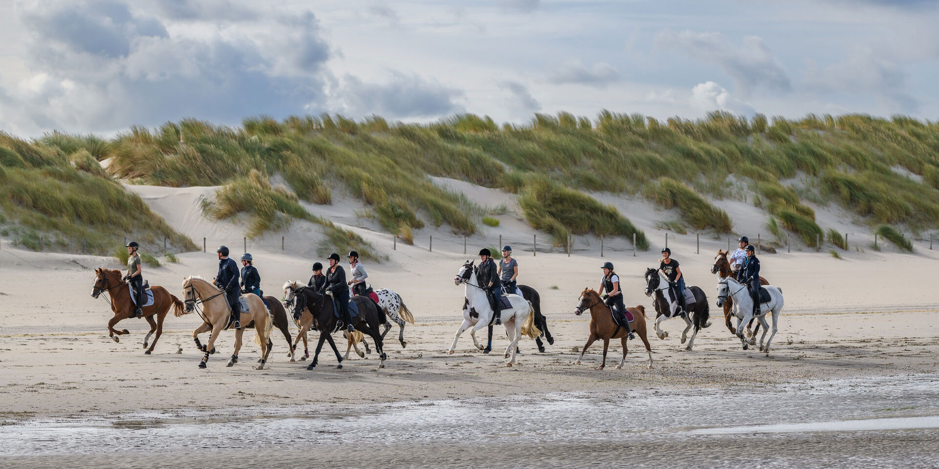 Groep ruiters op het strand van het Westland met op de voorgrond de zee en in de achtergrond de duinen in het Westland