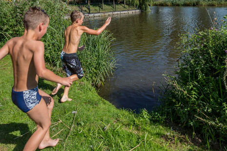 Jonge jongens die een aanloop nemen om op een zomerse dag een duik te nemen in het meer van recreatiegebied Het Prinsenbos in het Westland