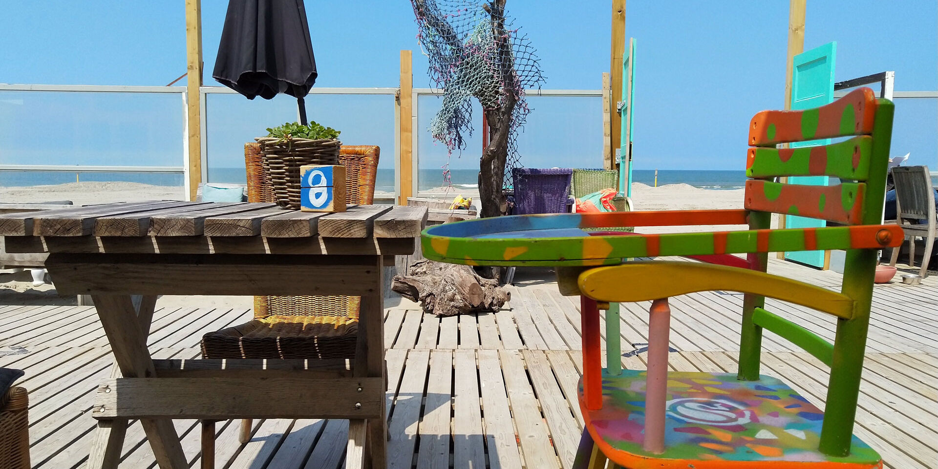 terras van strandtent Dreams Beach House met felgekleurde houten stoel en uitzicht op het strand en de zee in het Westland