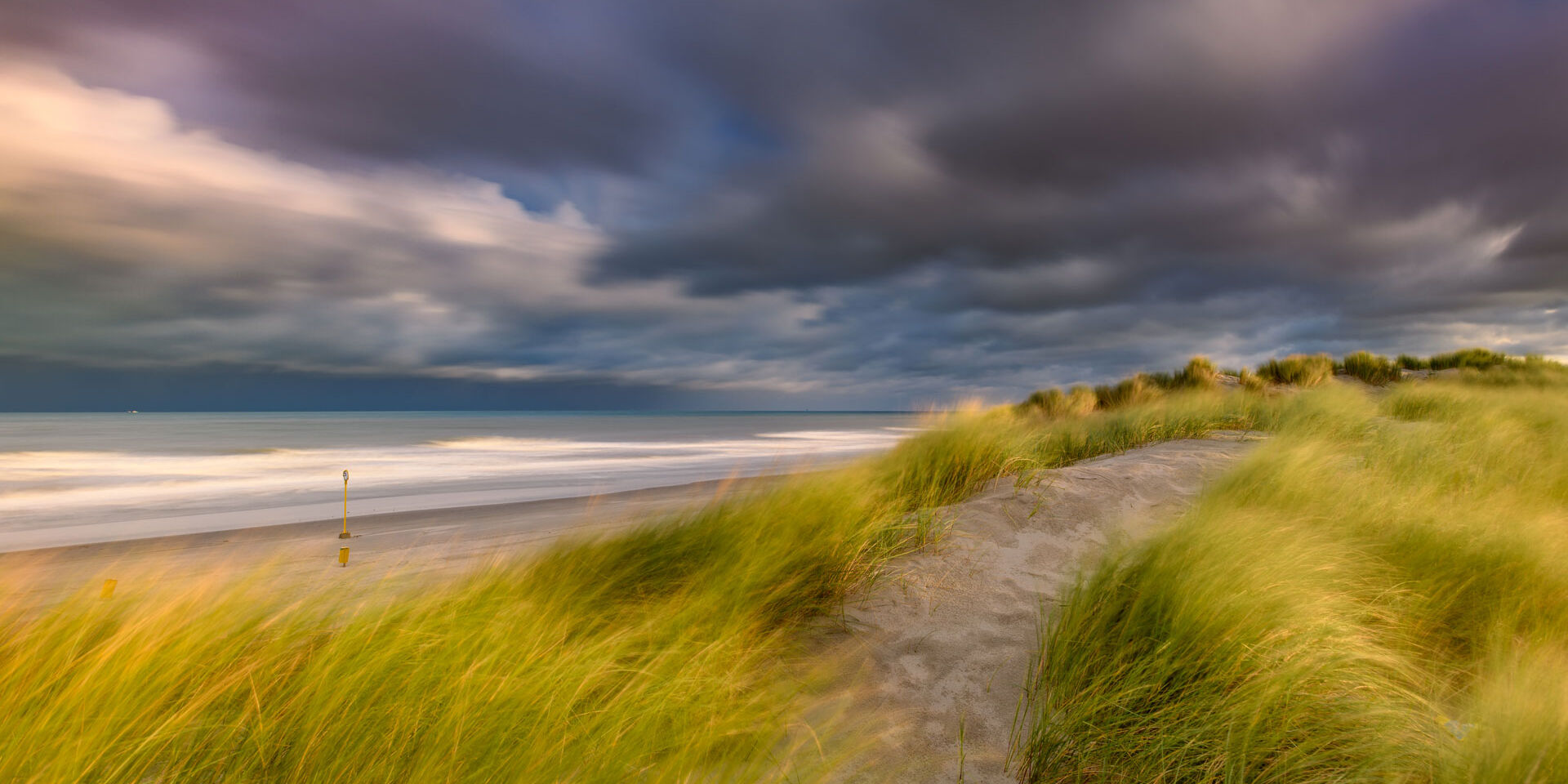 Duinen met groen helmgras met op de achtergrond het lege Westlandse strand en een donkere dreigende wolkenlucht