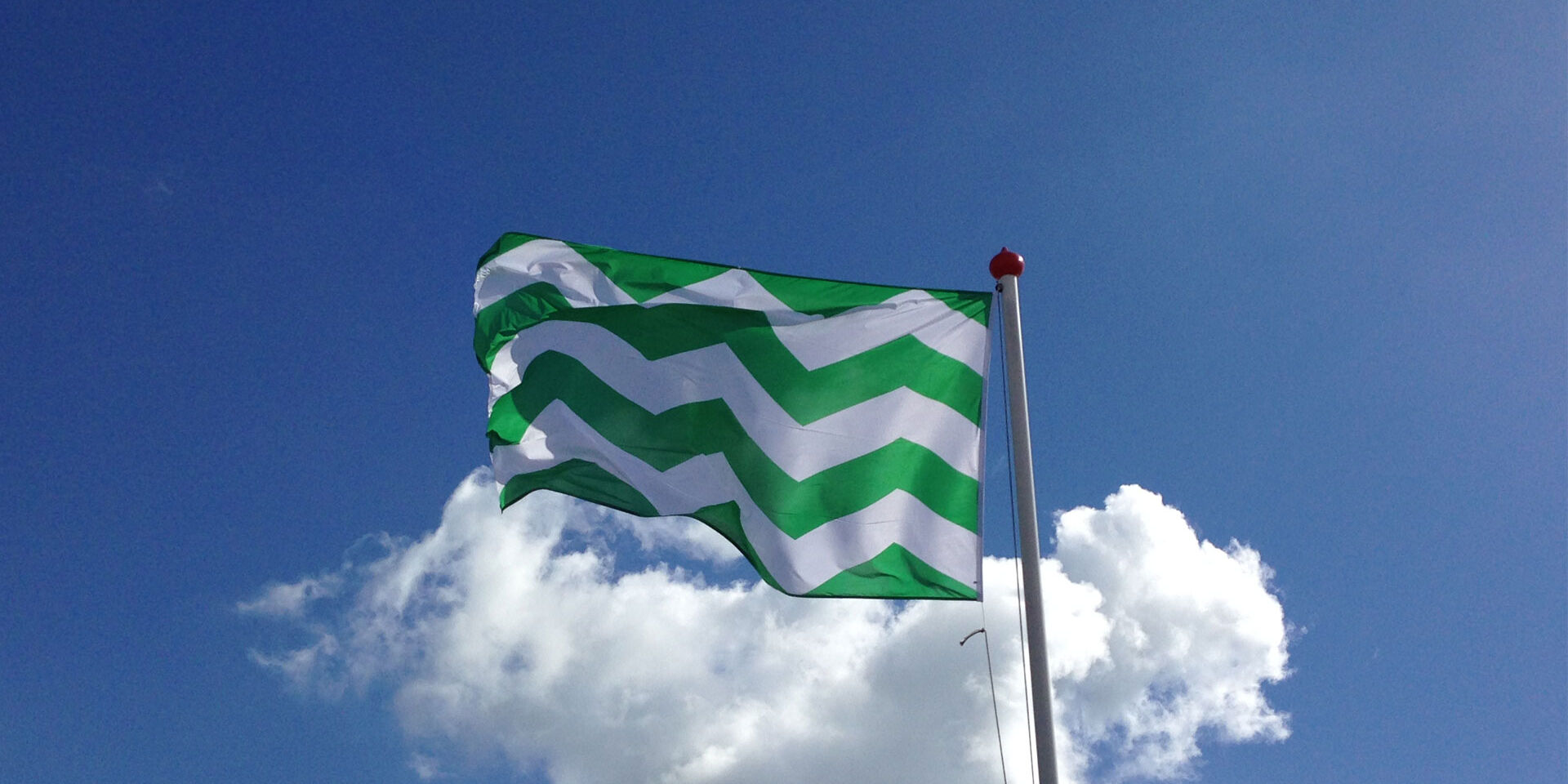 Westlandse vlag met groen witte gekartelde strepen aan vlaggenmast aan de Westlandse kust met blauwe lucht en witte wolken