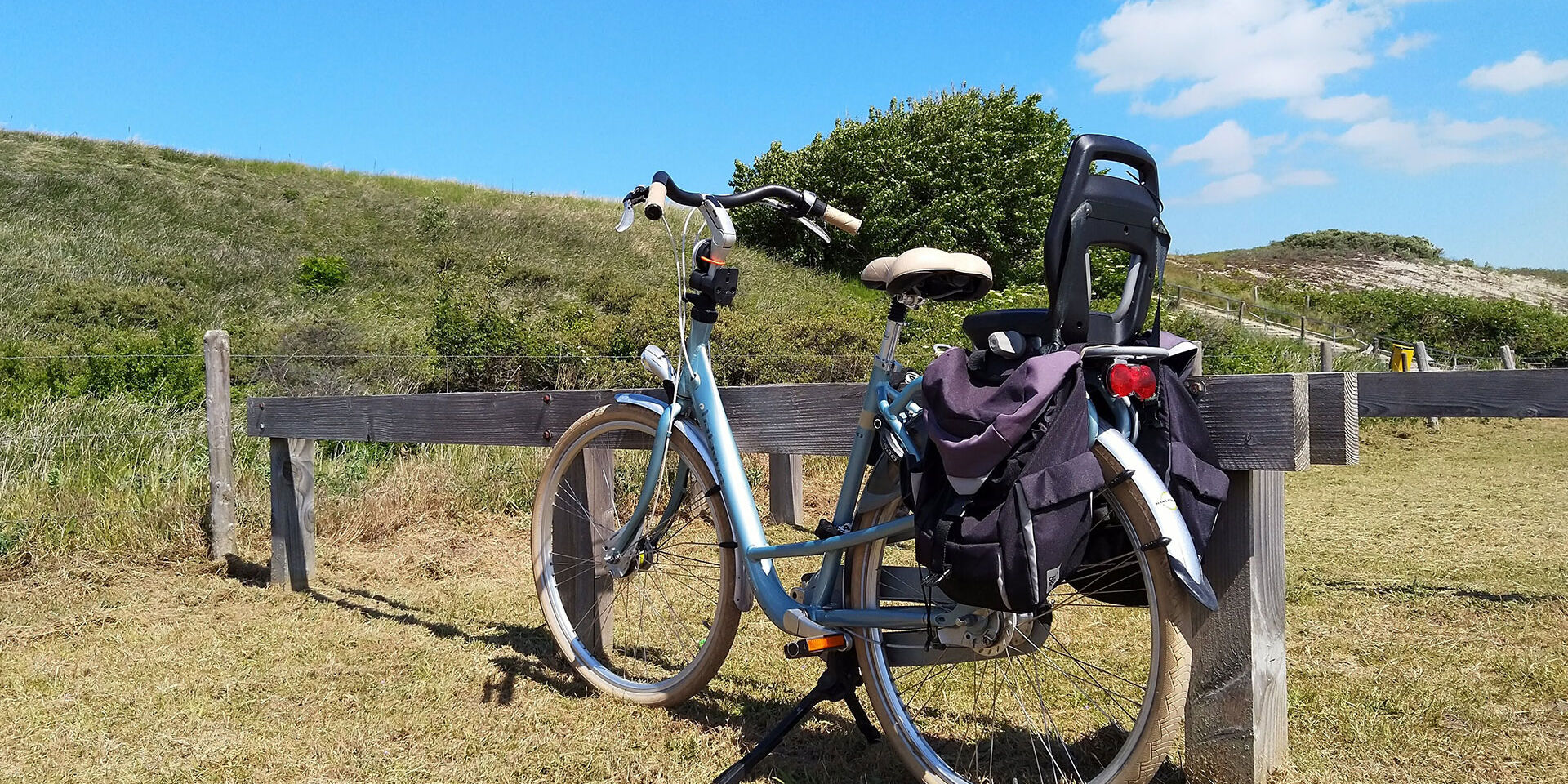blauwe fiets met kinderszitje geparkeerde onderaan de duinen bij strandopgang Strandweg bij Ter Heijde in het Westland