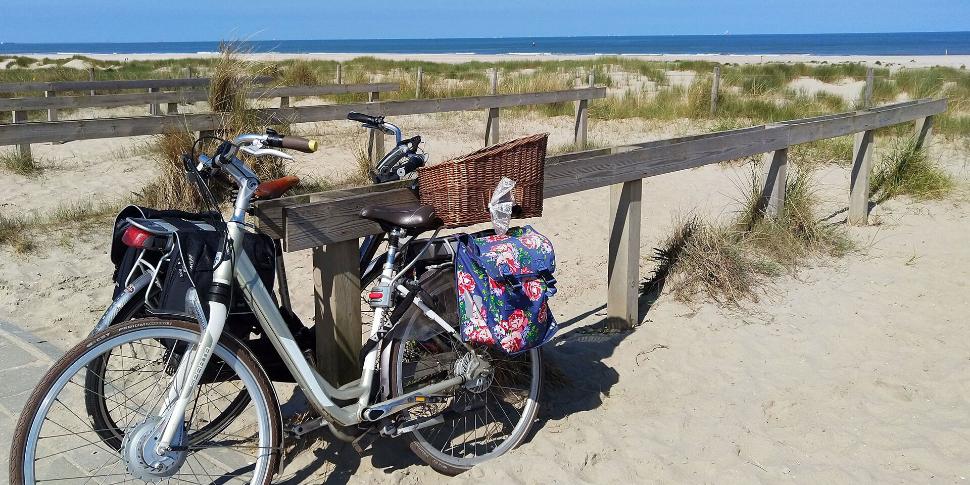 twee fietsen met fleurige fietstassen geparkeerd tegen een houten hek bij slag Molenslag aan het strand in het westland