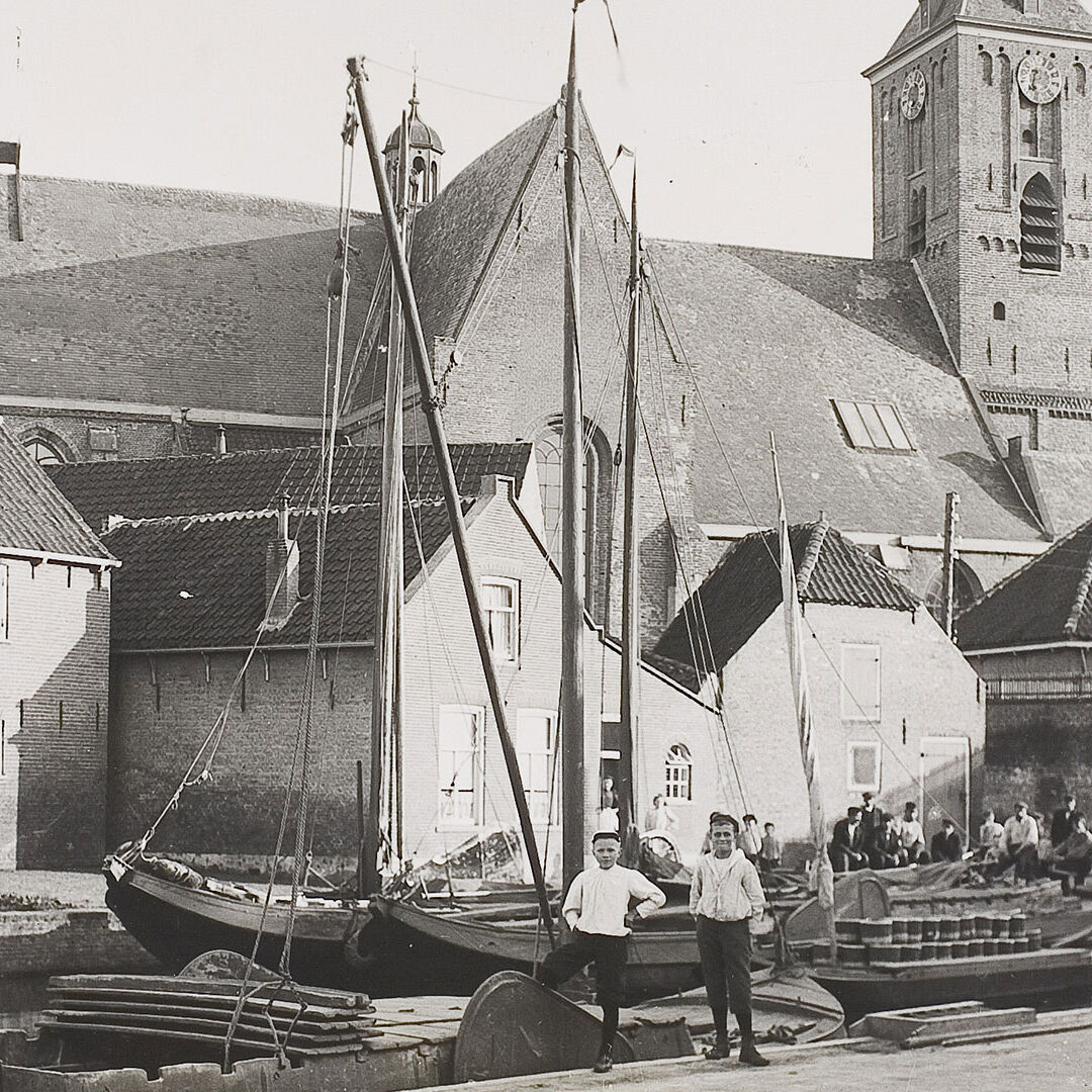 historische zwart-wit foto van de oude haven van naaldwijk in het westland met oude boten in de achtergrond en de kerktoren van Naaldwijk met op de voorgrond 2 mannen