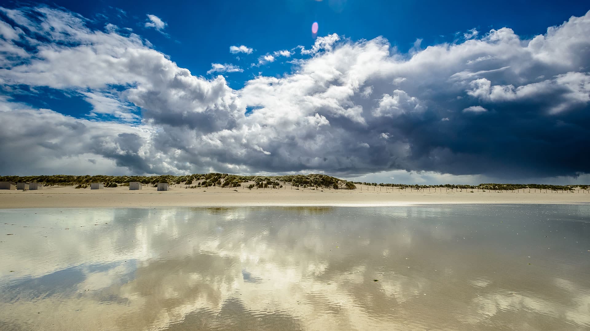 foto vanuit de zee richten de kust en duinen van het westland met een leeg strand, witte houten huisjes op het strand en grote witte wolken boven land