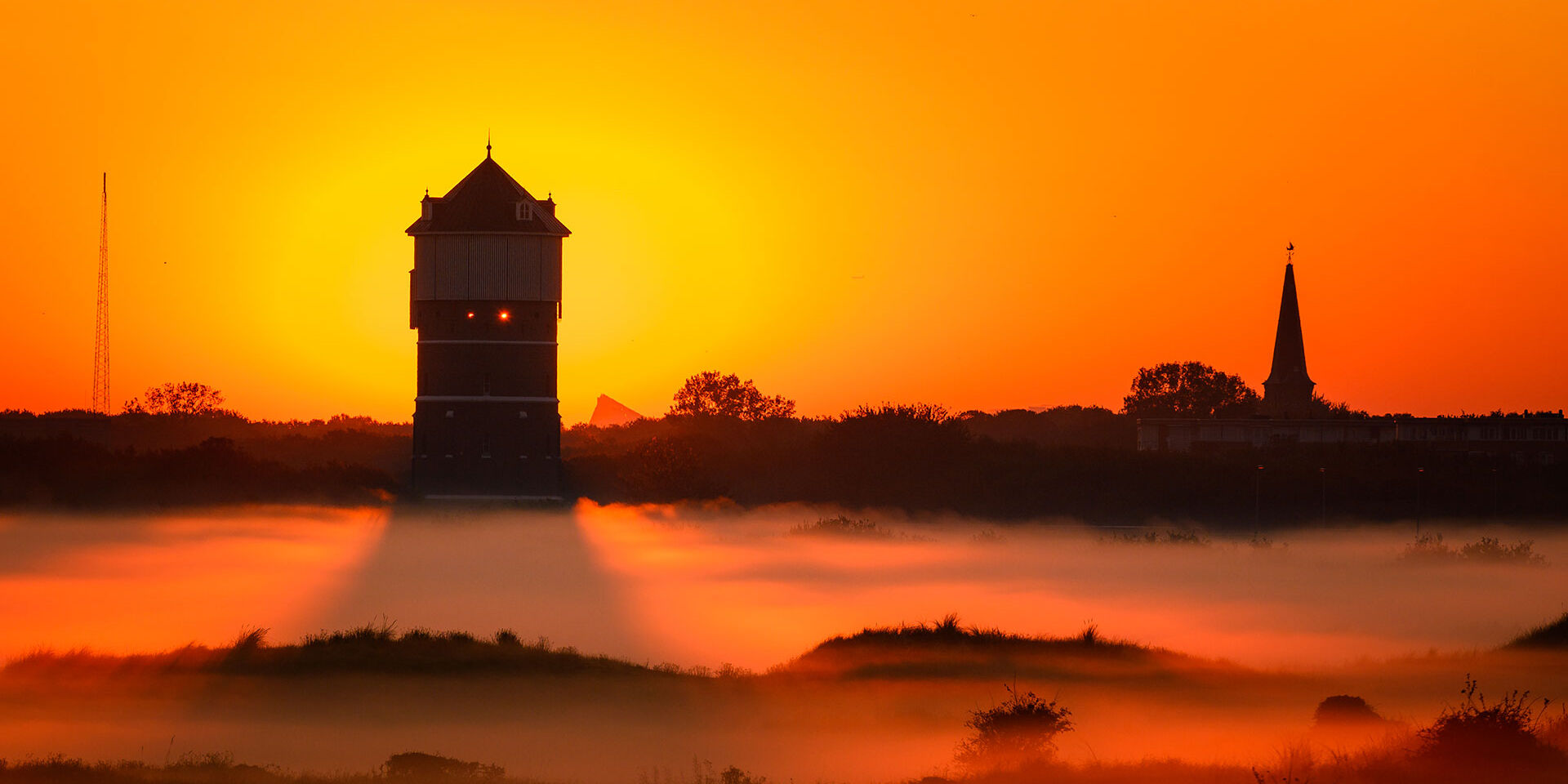 watertoren in duingebied Solleveld en Slag Molenslag aan de kust in het Westland met rode ondergaande zon en mist in de duinen