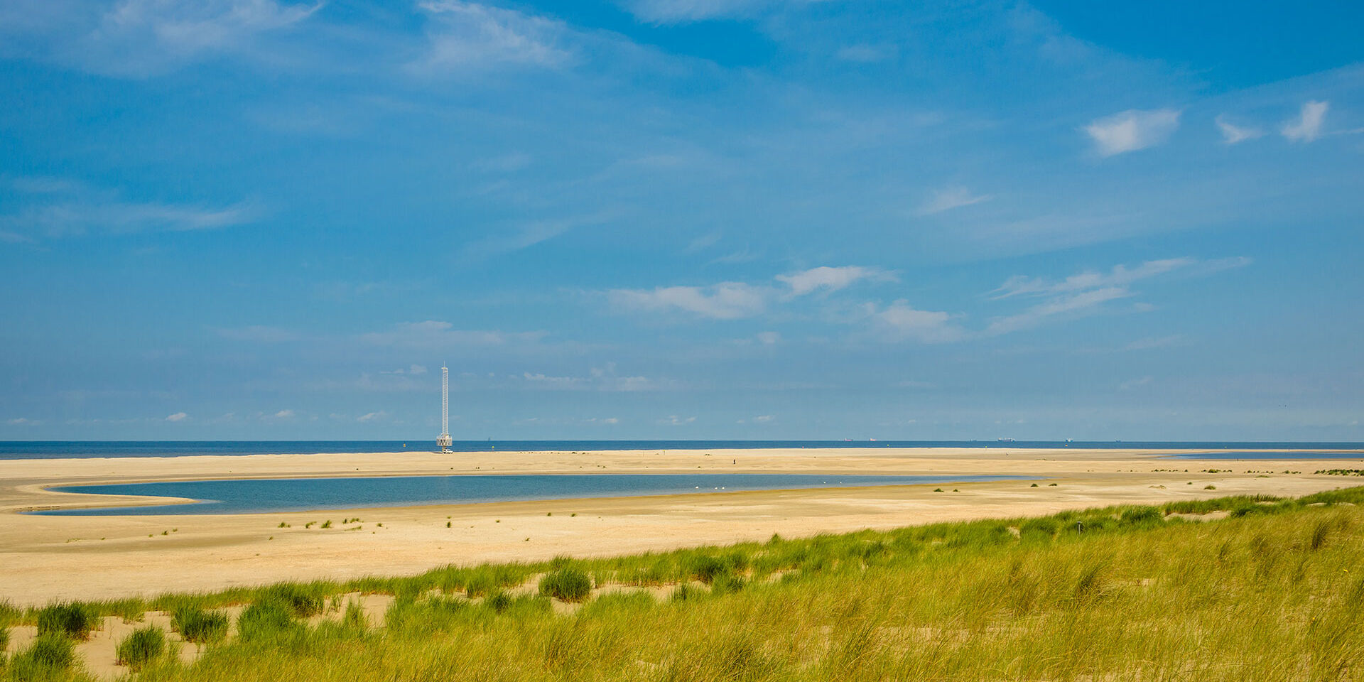 foto van een zonnig strand en duinen met in de achtergrond de Zandmotor in het Westland