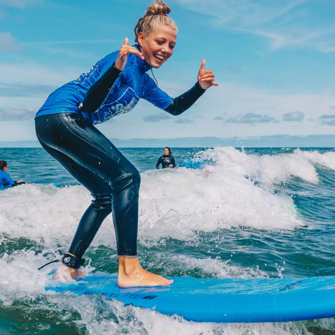 jonge vrouw staat op een blauwe golfplank in de branding van de zee in het westland tijdens een les golfsurfen van Dutch Surf Academy