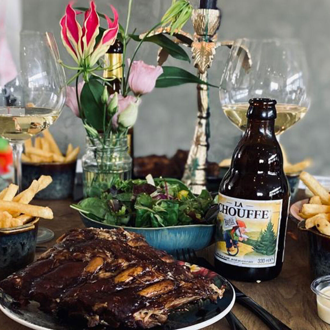 spareribs op tafel met frietjes en een flesje bier en een glas witte wijn op een bruine tafel bij Bistro De Herberg in het Westland