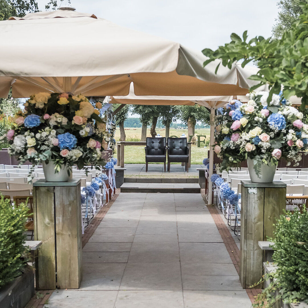 achtertuin van Brasserie Oostgaag versierd als trouwloctie met bloemen aan het gangpad en stoelen voor bruid en bruidegom en daarachter het voor LOVE op een grasveld bij trouwlocaties Brasserie Oostgaag in Midden-Delfland