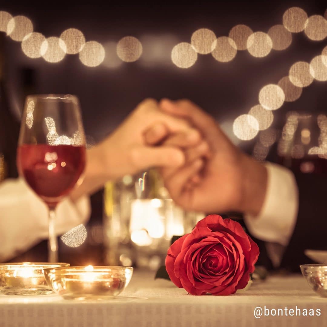 handen vasthouden glas rode wijn rode roos valentijn romantisch diner