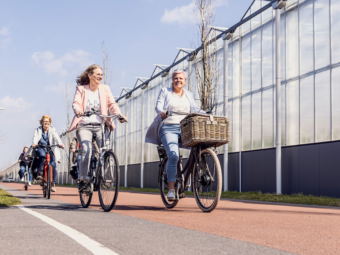 groepje dames fiets langs glazen kassen in het Westland tijdens een Kassen Route Westland langs glastuinbouwbedrijven